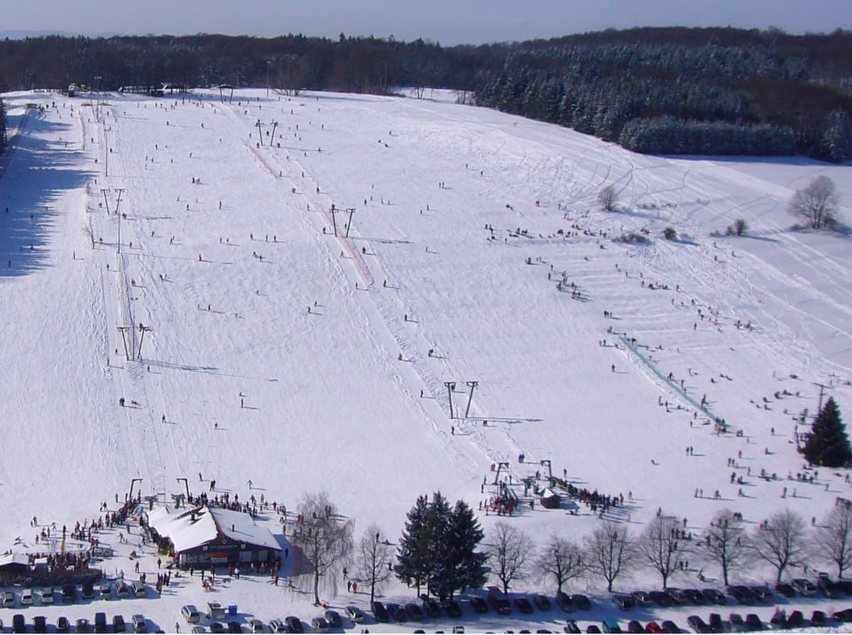 Skigebiet mit vielen Menschen, die auf der Piste Ski fahren und snowboarden.